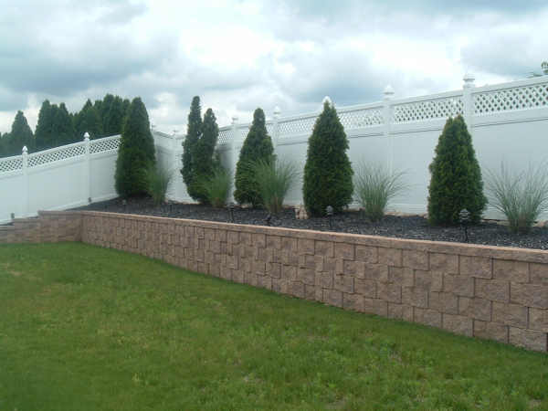 A yard with a white fence and shrubs.