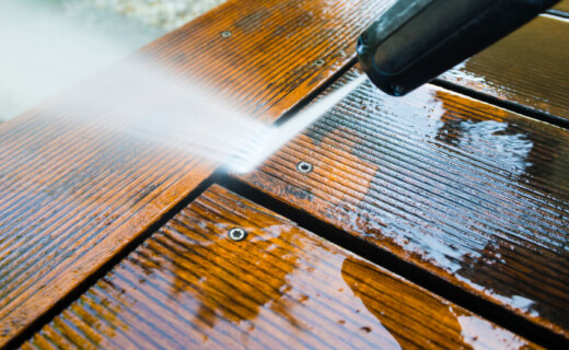 A man using a pressure washer to clean a wooden table.