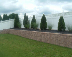 A yard with a white fence and shrubs.