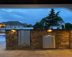 An outdoor kitchen with a fireplace and outdoor lighting.