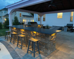 An outdoor kitchen with stools and lighting.